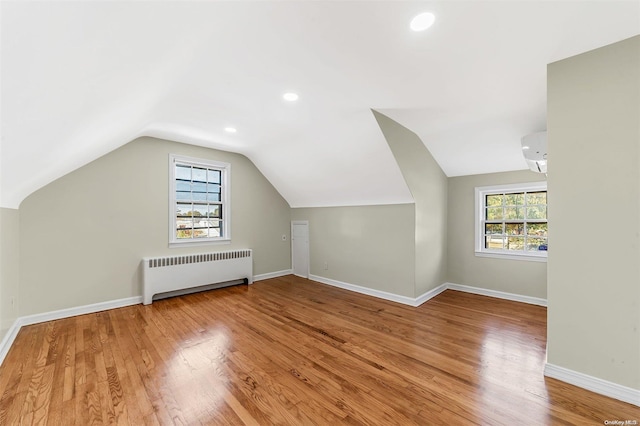 additional living space featuring wood-type flooring, vaulted ceiling, radiator, and a wall unit AC