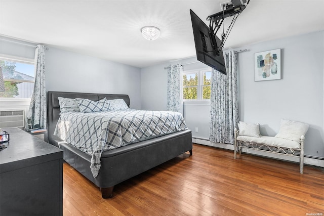 bedroom with multiple windows, wood-type flooring, and a baseboard radiator