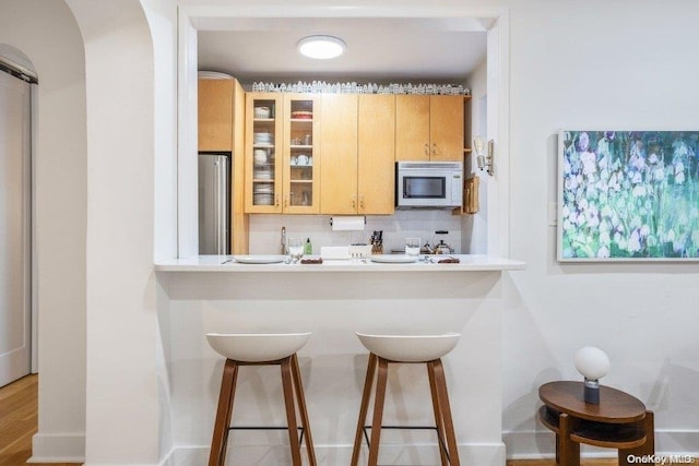 kitchen with a breakfast bar, light brown cabinets, decorative backsplash, stainless steel fridge, and light hardwood / wood-style floors