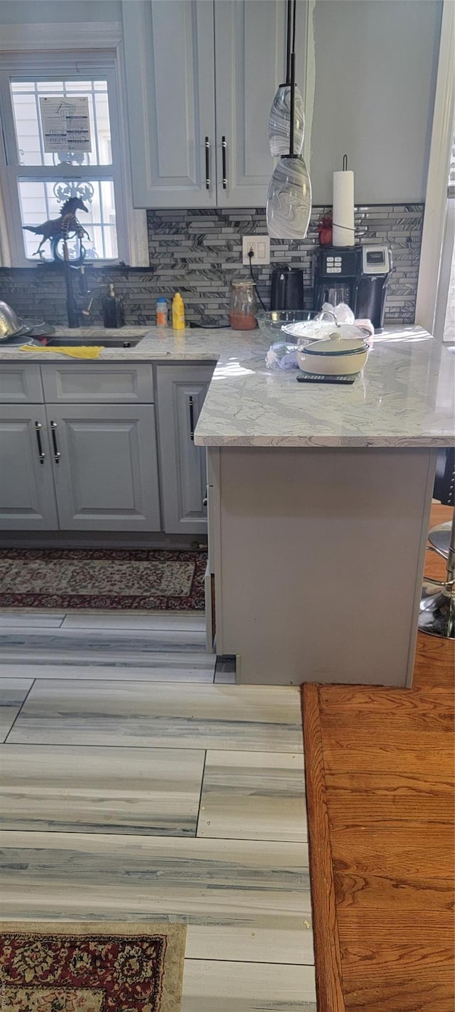 kitchen featuring tasteful backsplash, gray cabinetry, light stone counters, and pendant lighting