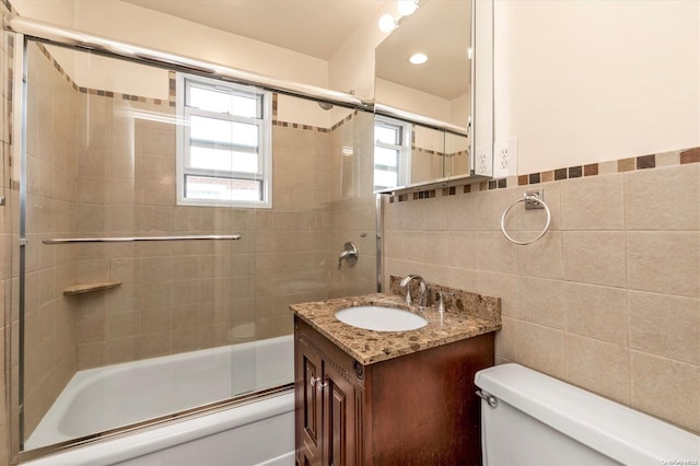 full bathroom with vanity, bath / shower combo with glass door, tile walls, and toilet