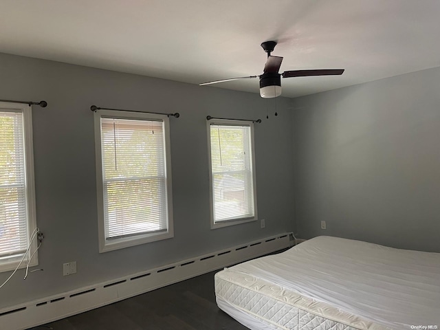 bedroom featuring dark wood-type flooring, multiple windows, a baseboard heating unit, and ceiling fan