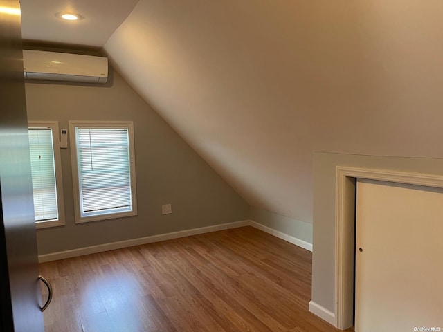 bonus room with lofted ceiling, light wood-type flooring, and an AC wall unit