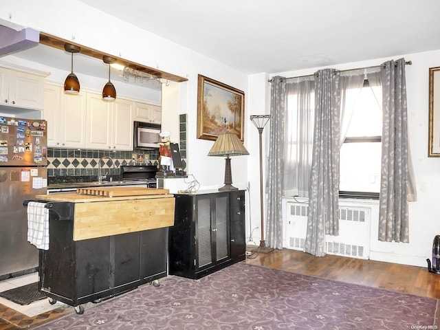 kitchen with hardwood / wood-style floors, stainless steel appliances, radiator, and pendant lighting