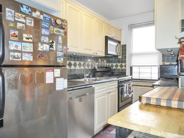 kitchen with sink, wooden counters, backsplash, cream cabinets, and appliances with stainless steel finishes