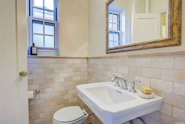 bathroom featuring toilet, sink, a wealth of natural light, and tile walls