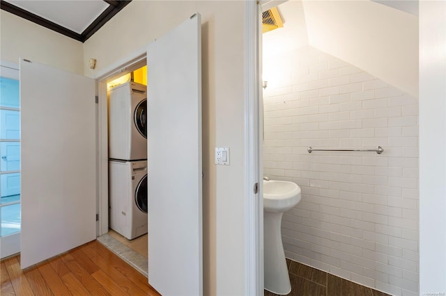 bathroom with hardwood / wood-style flooring, stacked washer / drying machine, and tile walls