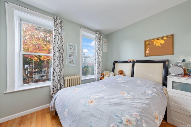 bedroom featuring radiator heating unit, light hardwood / wood-style flooring, and multiple windows