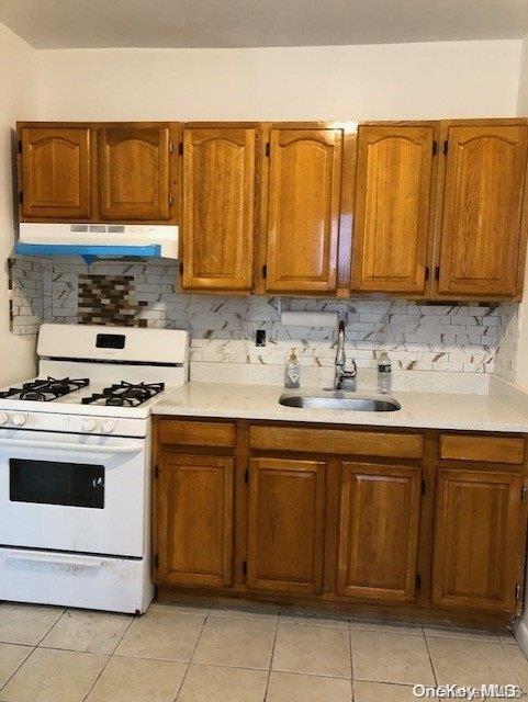 kitchen featuring white gas range, decorative backsplash, and light tile patterned floors