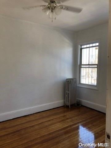 empty room featuring dark hardwood / wood-style flooring, ceiling fan, and radiator heating unit