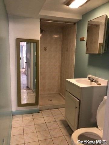 bathroom featuring tile patterned flooring, vanity, toilet, and a tile shower