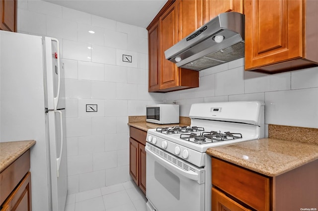 kitchen featuring white appliances, exhaust hood, light tile patterned floors, light stone countertops, and tile walls