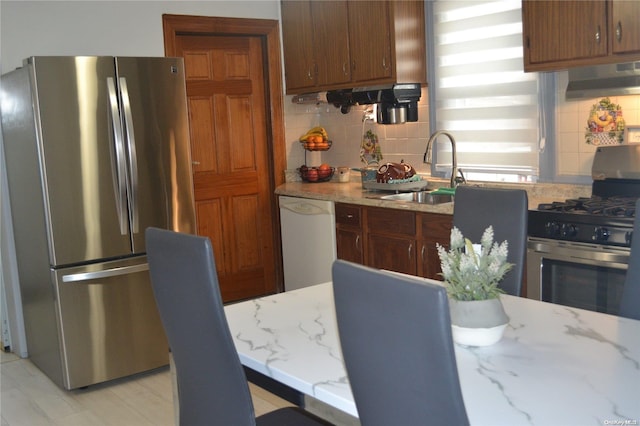 kitchen with ventilation hood, sink, tasteful backsplash, light stone counters, and stainless steel appliances