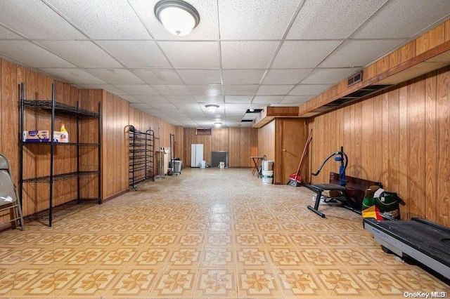 exercise room featuring a paneled ceiling and wood walls