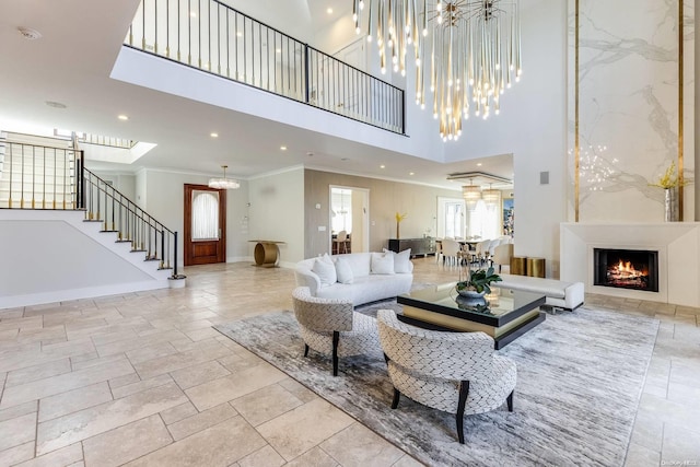 living room featuring a large fireplace, ornamental molding, a high ceiling, and an inviting chandelier