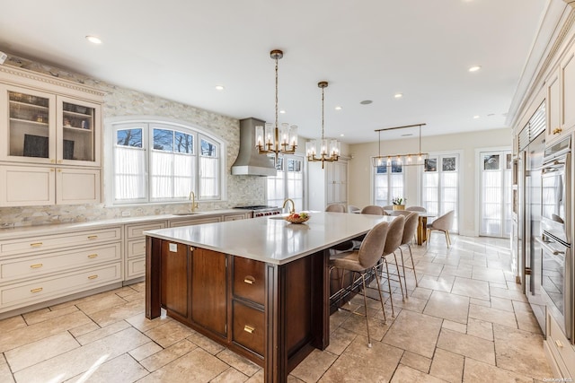 kitchen featuring wall chimney exhaust hood, decorative light fixtures, decorative backsplash, a breakfast bar, and a kitchen island