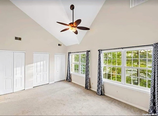 unfurnished bedroom featuring light carpet, two closets, high vaulted ceiling, and ceiling fan