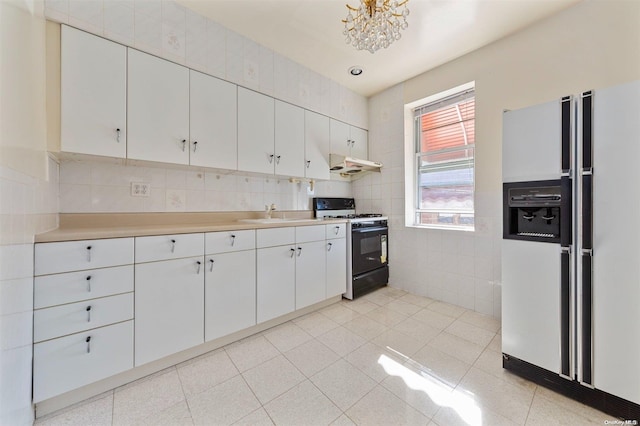 kitchen featuring white refrigerator with ice dispenser, white cabinets, exhaust hood, and black gas range oven