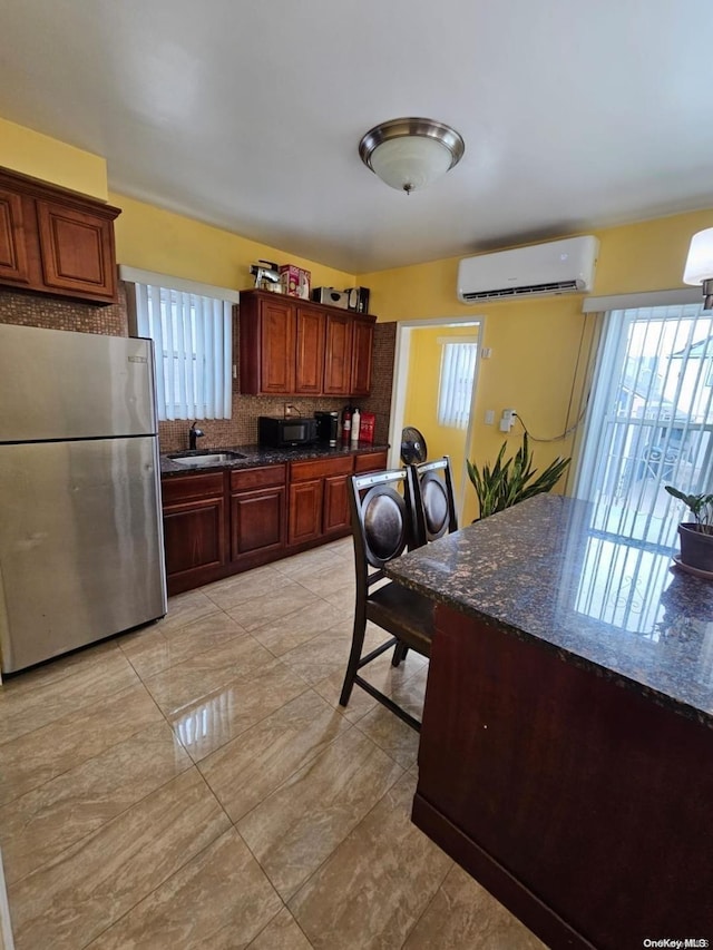 kitchen featuring sink, tasteful backsplash, a wall mounted AC, stainless steel fridge, and dark stone counters