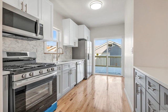 kitchen with decorative backsplash, white cabinets, light hardwood / wood-style floors, and appliances with stainless steel finishes