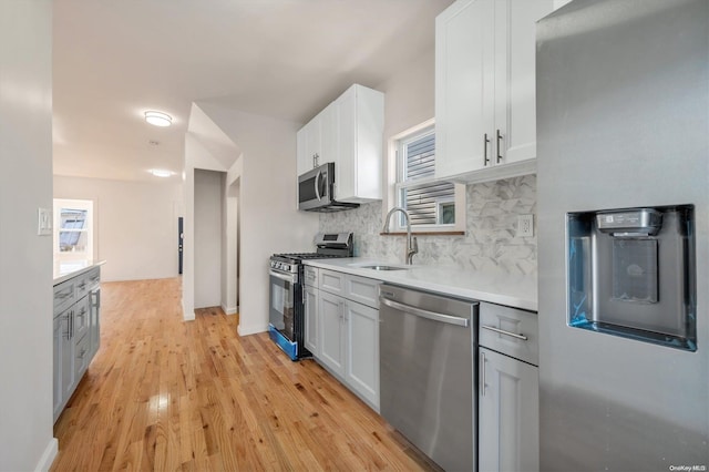 kitchen featuring appliances with stainless steel finishes, light wood-type flooring, backsplash, sink, and white cabinetry