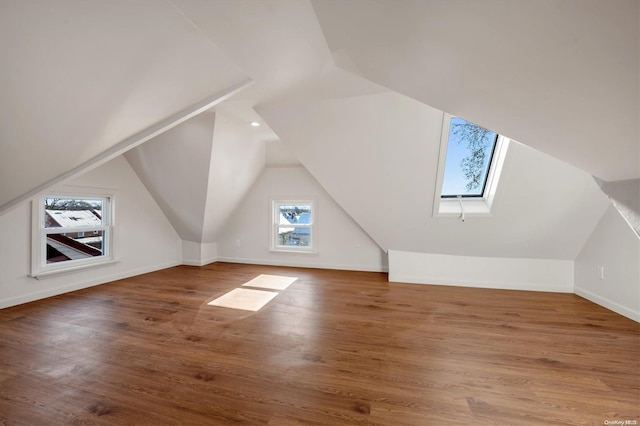 additional living space featuring wood-type flooring and lofted ceiling with skylight