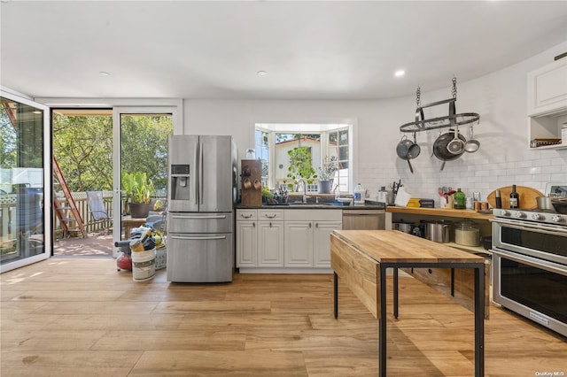 4 Maple St, Glenwood Landing, NY 11547 - kitchen with appliances with stainless steel finishes, a sink, decorative backsplash, light wood finished floors, and white cabinetry