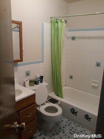 full bathroom with shower / bath combo, tile patterned flooring, toilet, vanity, and tile walls