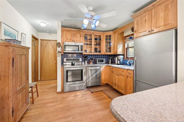 kitchen featuring backsplash, ceiling fan, light wood-type flooring, and stainless steel appliances