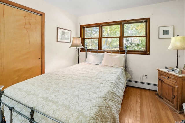 bedroom featuring a closet, light hardwood / wood-style flooring, and a baseboard heating unit