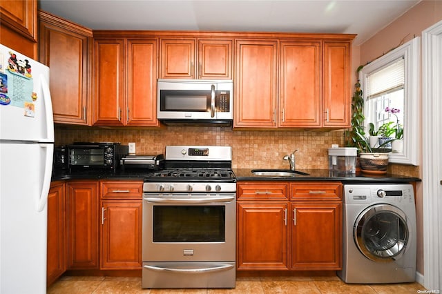 kitchen with appliances with stainless steel finishes, washer / clothes dryer, dark stone countertops, and sink