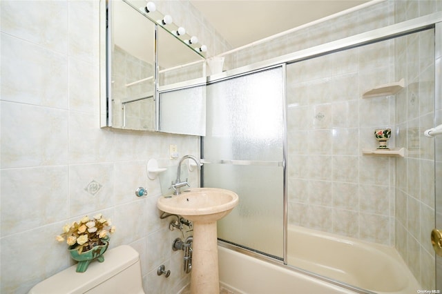 bathroom with combined bath / shower with glass door, tile walls, and toilet