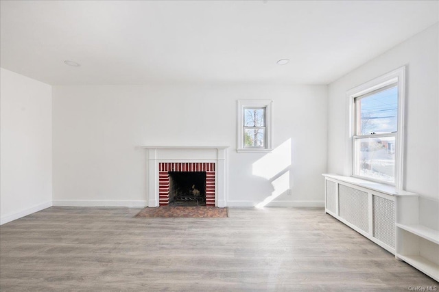 unfurnished living room featuring a fireplace, radiator heating unit, and light wood-type flooring