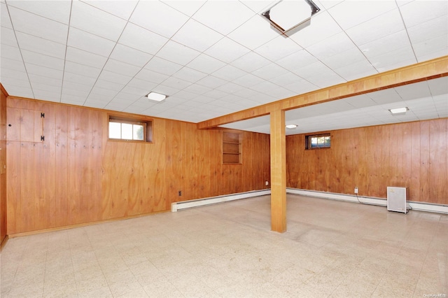 basement with a drop ceiling, baseboard heating, and wooden walls