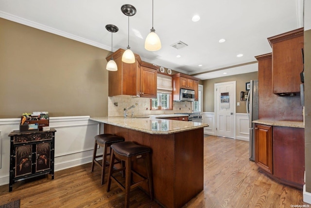 kitchen with kitchen peninsula, appliances with stainless steel finishes, light stone countertops, light hardwood / wood-style floors, and hanging light fixtures