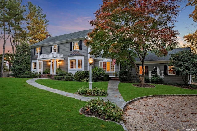 colonial inspired home featuring a balcony and a yard