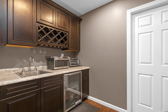 bar featuring dark wood-type flooring, sink, beverage cooler, and dark brown cabinets