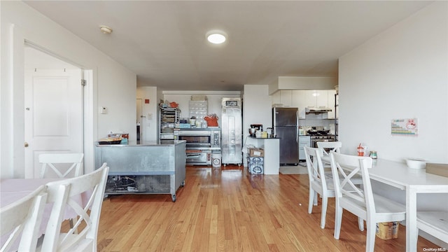 kitchen featuring stainless steel appliances, backsplash, light wood-style flooring, and white cabinetry