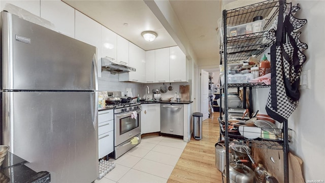 kitchen with light wood finished floors, stainless steel appliances, white cabinets, under cabinet range hood, and dark countertops