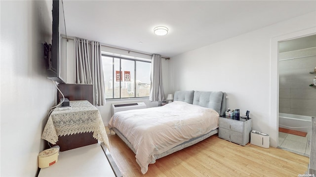 bedroom with wood-type flooring, an AC wall unit, and connected bathroom