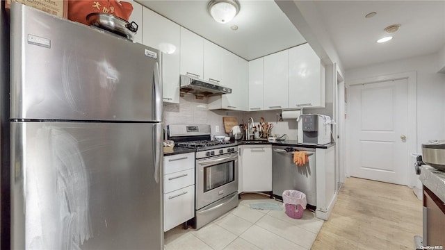 kitchen with under cabinet range hood, stainless steel appliances, dark countertops, and white cabinets