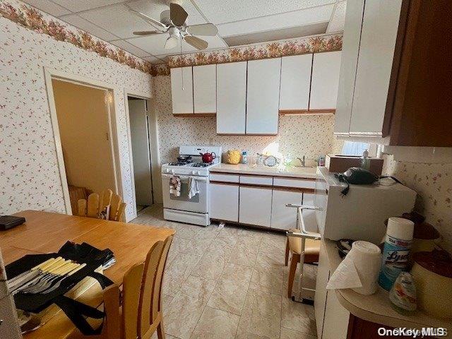 kitchen featuring a paneled ceiling, white range oven, ceiling fan, sink, and white cabinets