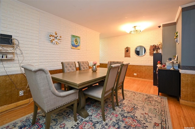 dining room featuring crown molding, brick wall, and light wood-type flooring