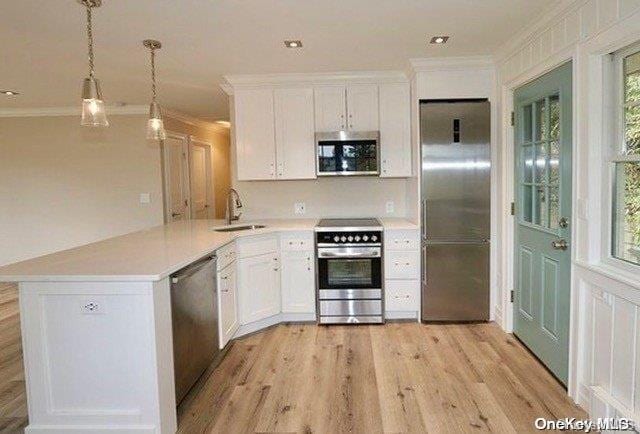 kitchen featuring kitchen peninsula, stainless steel appliances, sink, decorative light fixtures, and white cabinetry