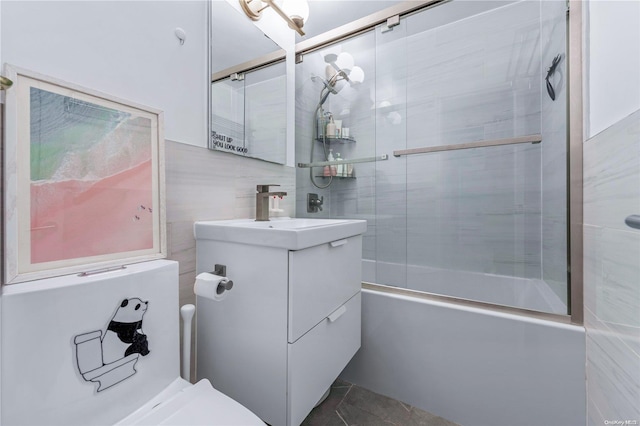 full bathroom with vanity, bath / shower combo with glass door, tile patterned flooring, toilet, and tile walls