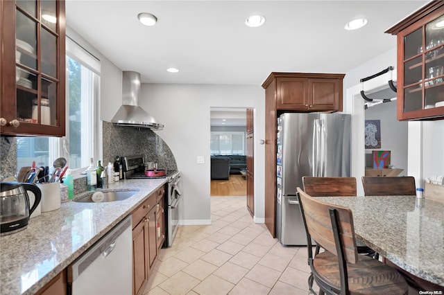 kitchen with light stone countertops, stainless steel appliances, wall chimney range hood, decorative backsplash, and light tile patterned flooring