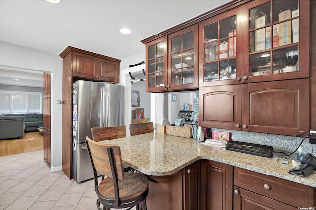 kitchen featuring light stone countertops, backsplash, stainless steel fridge, a kitchen bar, and light tile patterned floors