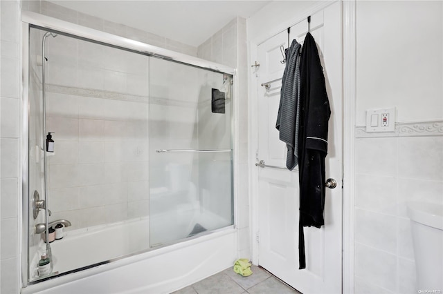 bathroom featuring tile patterned flooring, toilet, shower / bath combination with glass door, and tile walls