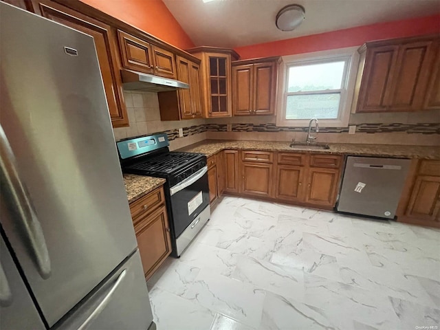 kitchen with backsplash, sink, vaulted ceiling, light stone countertops, and appliances with stainless steel finishes