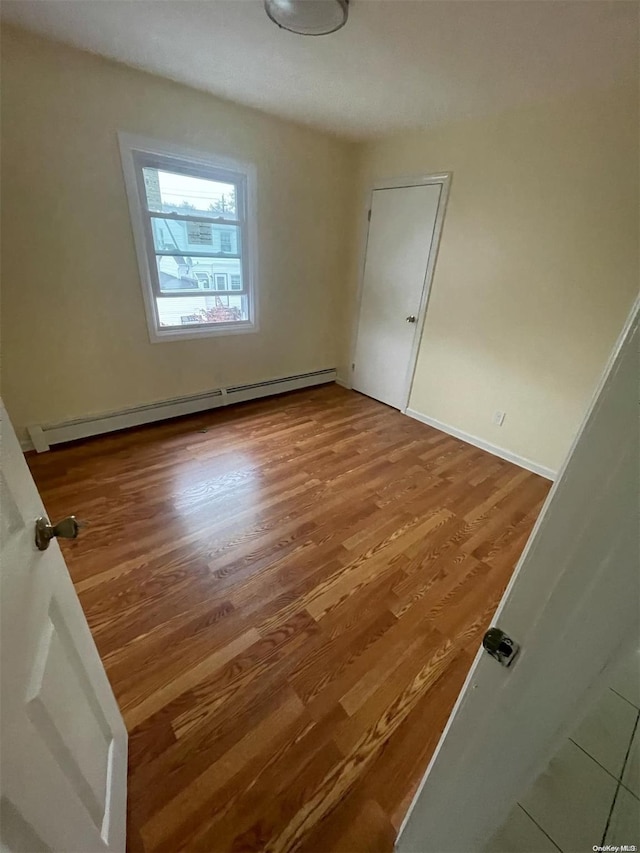 empty room featuring wood-type flooring and a baseboard heating unit